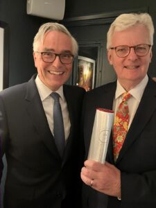 A portrait photograph of Jonathan Davis holding his Best Broadcast Journalist 2024 award from the AIC, with original co-host Simon Elliott to his right.